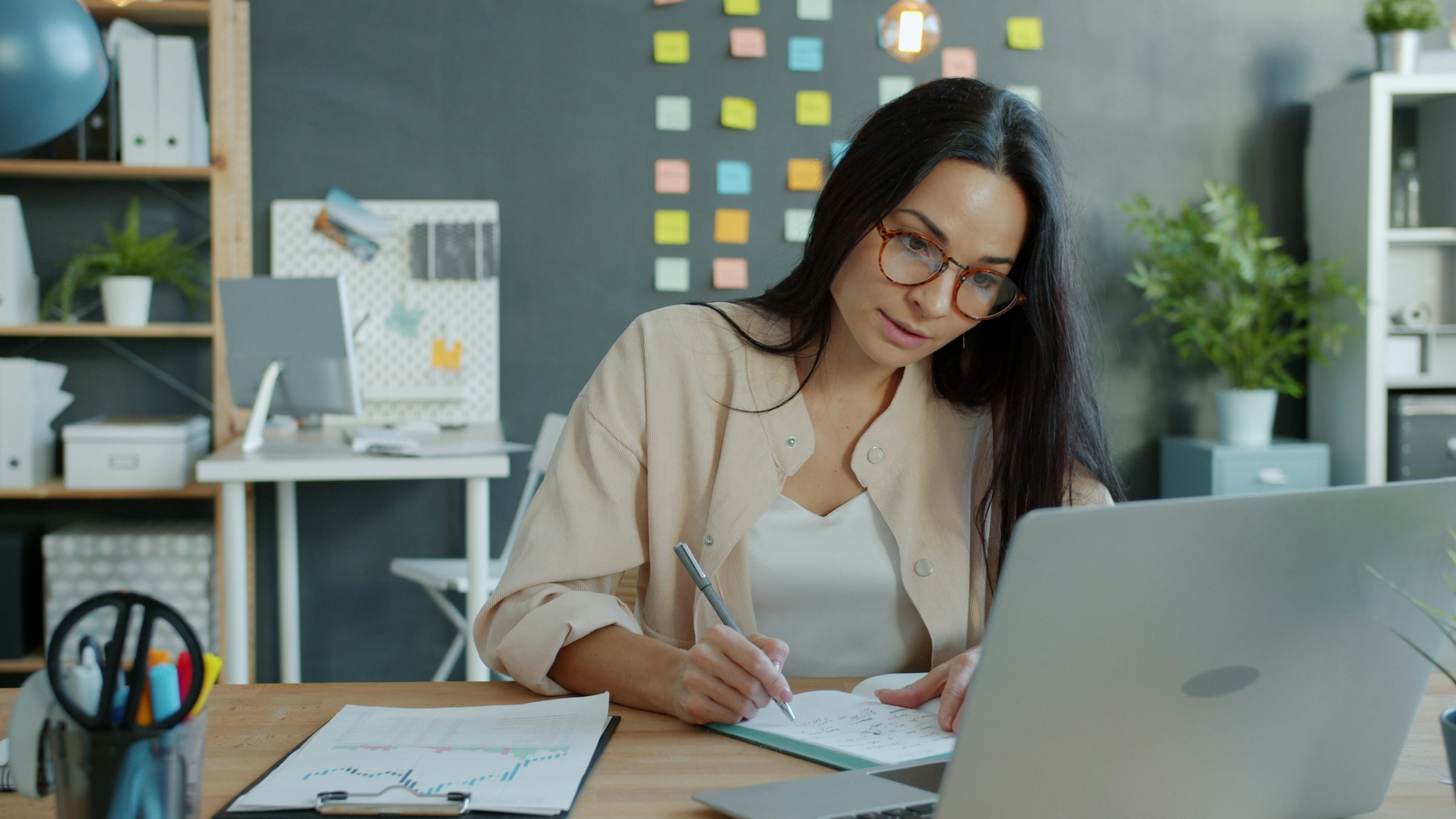 Young professional woman taking notes while learning online